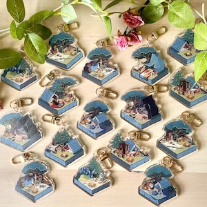 Puede incluir: Una colección de llaveros con temática de camping. Cada llavero presenta una escena de campamento en miniatura con una tienda de campaña, árboles y equipo de campamento. Los llaveros tienen un cierre dorado y están hechos de acrílico transparente con ilustraciones coloridas.