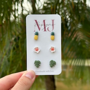 May include: A set of six stud earrings featuring three different designs: pineapples, flowers, and monstera leaves. The earrings are handmade and come on a white card with the text "MJ Designs" and "Handmade with love".
