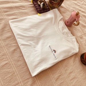 Peut inclure: T-shirt blanc avec un graphique arc-en-ciel et le texte "Rainbow Warrior" imprimé sur le devant.