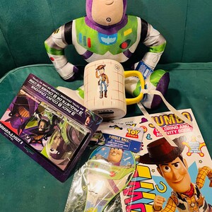 May include: A collection of Toy Story merchandise including a Buzz Lightyear plush, a Woody mug, a coloring book, crayons, and a paddle ball set. The items feature vibrant colors and character designs from the animated film.