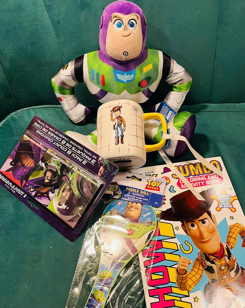 May include: A collection of Toy Story merchandise including a Buzz Lightyear plush, a Woody mug, a coloring book, crayons, and a paddle ball set. The items feature vibrant colors and character designs from the animated film.