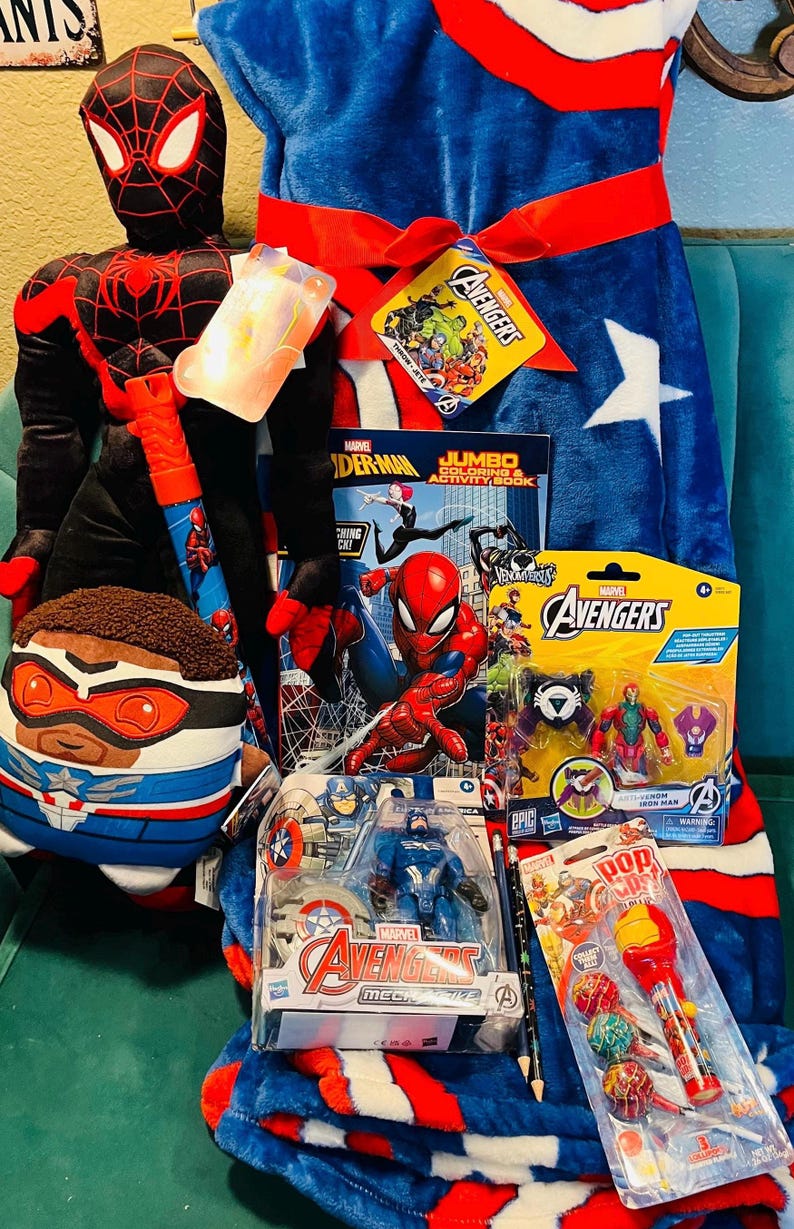 May include: A collection of Marvel Avengers merchandise, including a plush Spider-Man, a Captain America pillow, a blue and red blanket, action figures, a coloring book, and a lollipop. The items are arranged on a teal surface.