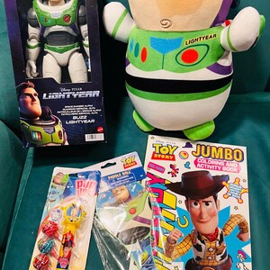 May include: A collection of Toy Story merchandise, including a Buzz Lightyear action figure in a box, a plush Buzz Lightyear, a coloring book, lollipops, and a paddle ball toy. The items are arranged on a teal surface.
