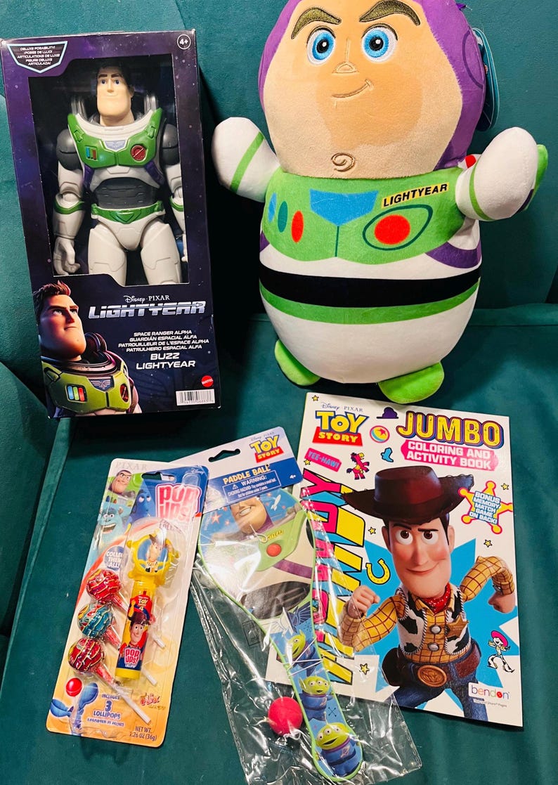May include: A collection of Toy Story merchandise, including a Buzz Lightyear action figure in a box, a plush Buzz Lightyear, a coloring book, lollipops, and a paddle ball toy. The items are arranged on a teal surface.