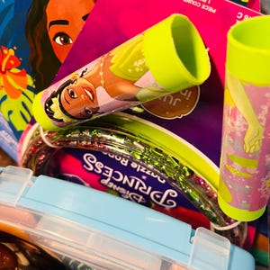 Puede incluir: Una colecci&oacute;n de art&iacute;culos para ni&ntilde;os, que incluye un libro para colorear con un personaje de dibujos animados, un estuche azul claro y varios tubos con dise&ntilde;os de princesas. Los tubos tienen tapas de color verde brillante.