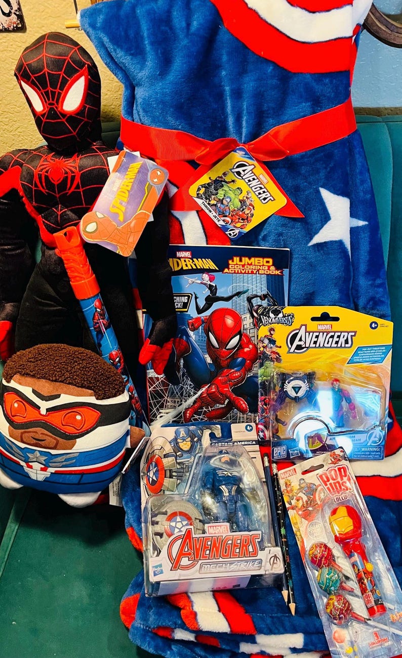May include: A collection of Marvel Avengers merchandise, including a Spider-Man plush, a Captain America action figure, a coloring book, and lollipops. The items are arranged on a blue blanket with a white star.