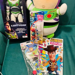 May include: A collection of Disney Pixar Lightyear themed toys. Includes a Buzz Lightyear action figure in a box, a plush Buzz Lightyear, a paddle ball set, a coloring book featuring Woody, and a lollipop set.