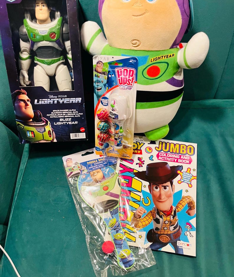 May include: A collection of Disney Pixar Lightyear themed toys. Includes a Buzz Lightyear action figure in a box, a plush Buzz Lightyear, a paddle ball set, a coloring book featuring Woody, and a lollipop set.