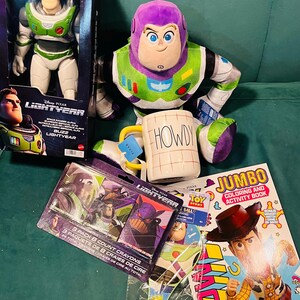 May include: A collection of Toy Story merchandise featuring Buzz Lightyear. Includes a Buzz Lightyear action figure in a box, a plush Buzz Lightyear, a mug with "HOWDY" on it, crayons, a coloring book, and a Toy Story watch.