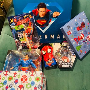 Peut inclure: Plusieurs articles sur le th&egrave;me des super-h&eacute;ros, dont un coffret Superman, des figurines et des jouets Spider-Man. Les articles sont dans des bo&icirc;tes et des emballages vari&eacute;s, avec des couleurs vives et des graphismes de personnages. Le texte "DC Studios" et "Avengers" est visible.
