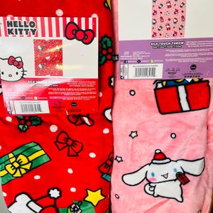 May include: Two Hello Kitty silk touch throws. One is red with white polka dots, Hello Kitty, bows, and Christmas decorations. The other is pink with stars, a gift, and a character wearing a Santa hat. Both throws have product packaging.