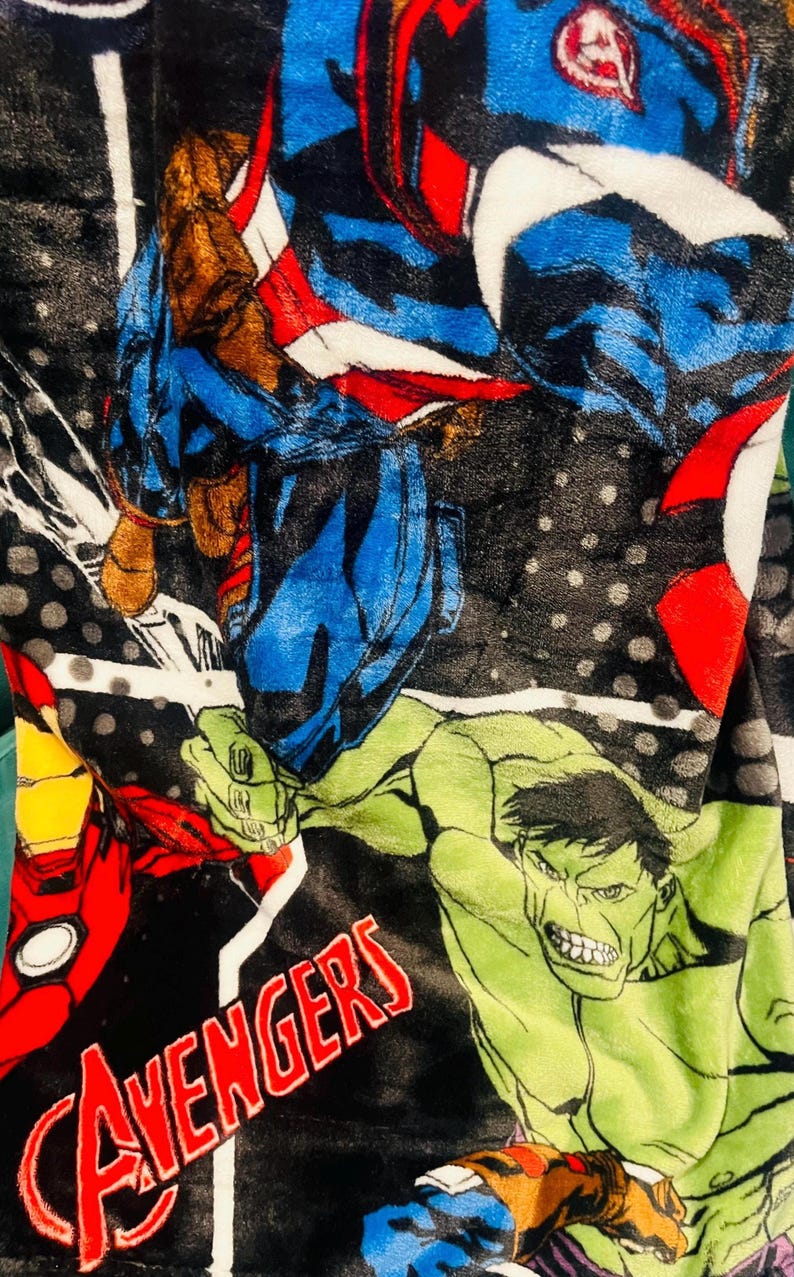 Peut inclure: Une couverture en peluche avec un design vibrant des personnages des Avengers. La couverture pr&eacute;sente Captain America, Iron Man, Hulk et d'autres h&eacute;ros dans des poses d'action sur un fond noir avec le mot "Avengers" en rouge.