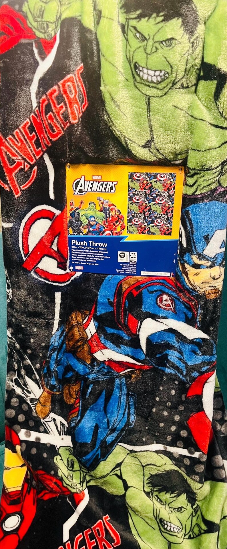 Peut inclure: Couverture en peluche avec les personnages des Avengers de Marvel, dont Hulk et Captain America, dans un style bande dessin&eacute;e. La couverture est noire avec des graphismes rouges, bleus, verts et blancs. Une bo&icirc;te avec le logo des Avengers est visible.