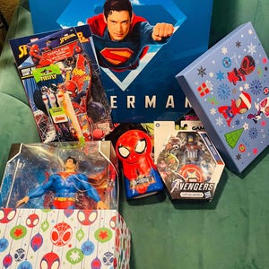 Peut inclure: Divers produits d&eacute;riv&eacute;s sur le th&egrave;me des super-h&eacute;ros, dont une bo&icirc;te Superman, des figurines et des articles sur le th&egrave;me de Spider-Man. La bo&icirc;te Superman pr&eacute;sente une image de Superman. D'autres articles incluent un jeu de pagaie Spider-Man et une figurine Captain America des Avengers.