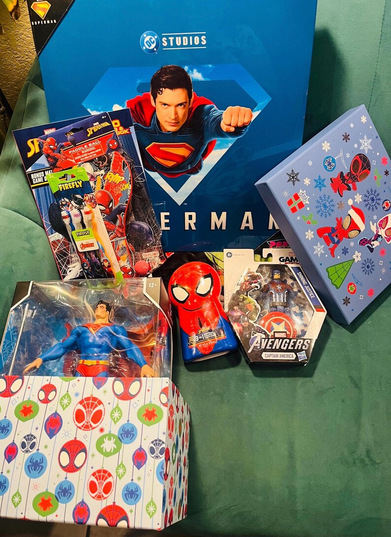 Peut inclure: Divers produits d&eacute;riv&eacute;s sur le th&egrave;me des super-h&eacute;ros, dont une bo&icirc;te Superman, des figurines et des articles sur le th&egrave;me de Spider-Man. La bo&icirc;te Superman pr&eacute;sente une image de Superman. D'autres articles incluent un jeu de pagaie Spider-Man et une figurine Captain America des Avengers.