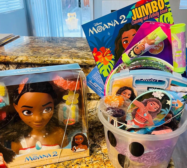 Puede incluir: Una cesta de regalo llena de art&iacute;culos tem&aacute;ticos de Moana. Incluye una mu&ntilde;eca de cabeza de peinado de Moana, un libro para colorear y actividades, una varita de burbujas y otros accesorios. La cesta es morada y blanca.