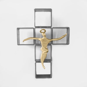 May include: A gold-colored sculpture of a person with outstretched arms, positioned within a gray metal frame shaped like a cross.