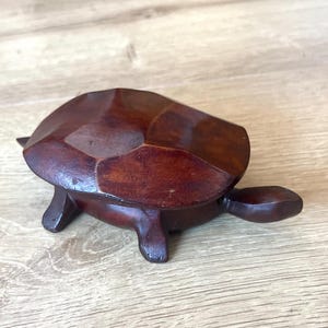 May include: A dark brown wooden turtle figurine with a polished, faceted shell. The sculpture features a smooth, rounded head and four short legs, showcasing the natural grain and deep, rich tones of the wood in a solid, carved construction.