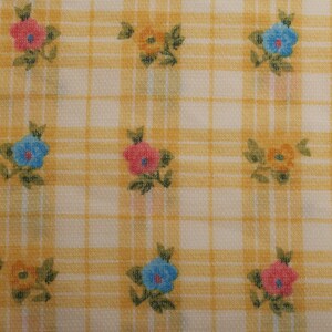 Puede incluir: Tela a cuadros amarillos y blancos con motivos florales. Las flores son rosas, azules y naranjas, con hojas verdes. La tela tiene un aspecto texturizado, adecuada para diversos proyectos de manualidades y costura.