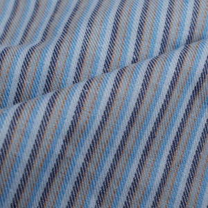 Op de afbeelding: Close-up van een stof met een diagonaal streepjespatroon. De strepen wisselen af tussen lichtblauw, marineblauw en bruin. De stof is licht gekreukt, wat suggereert dat hij zacht en soepel is. Het kleurenpalet is koel en gedempt.