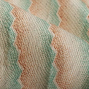 May include: Close-up of a fabric with a wavy striped pattern in shades of peach, green, and white.