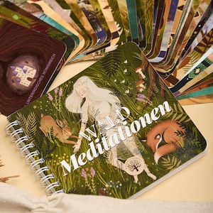 Könnte beinhalten: Ein Spiralbuch und ein Kartenspiel mit Naturmotiven. Das Journalcover zeigt eine Frau mit langen weißen Haaren, ein Kaninchen und einen schlafenden Fuchs. Die Worte "WALD Meditationen" sind auf dem Cover aufgedruckt.