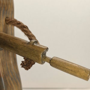 May include: A wooden figurine of a person holding a rifle. The figurine is made of dark brown wood and has a rope tied around its neck. The rifle is made of light brown wood and has a small, round barrel.