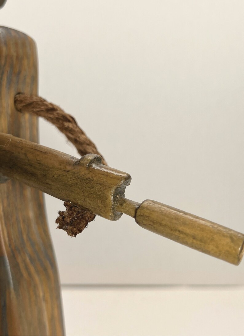May include: A wooden figurine of a person holding a rifle. The figurine is made of dark brown wood and has a rope tied around its neck. The rifle is made of light brown wood and has a small, round barrel.