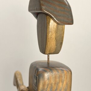 May include: Wooden figurine of a soldier wearing a hat with red, white, and blue stripes. The soldier is holding a rifle and has a rope tied around its waist. The figurine has a U.S. Army star on its chest.