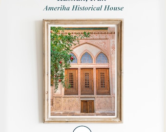 Könnte beinhalten: Ein gerahmtes Foto eines traditionellen iranischen Hauses mit aufwendigen Fliesenarbeiten und Holztüren. Das Haus ist von einem üppigen grünen Baum mit roten Früchten umgeben. Der Text "Kashan, Iran Ameritha Historical House" ist über dem Bild gedruckt.
