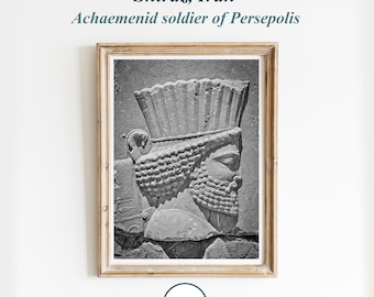 May include: A black and white photograph of a stone relief sculpture of an Achaemenid soldier from Persepolis, Iran. The soldier is wearing a tall, conical hat and has a beard. The sculpture is framed in a wooden frame.