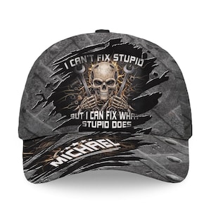 Op de afbeelding: Grijze baseballcap met een distressed design. De cap heeft een schedel met moersleutels, met de tekst "I CAN'T FIX STUPID BUT I CAN FIX WHAT STUPID DOES" en de naam "MICHAEL".