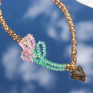May include: A gold chain necklace with a pink and green beaded flower charm and a gold heart pendant.