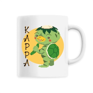 Peut inclure: Une tasse en céramique blanche avec une illustration verte et jaune d'un kappa, un esprit d'eau japonais, tenant un concombre. Le texte "KAPPA" est écrit en noir sur le côté gauche de la tasse.
