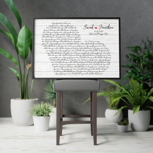 May include: A white wood sign with black calligraphy text that reads "Any song you hear,  I'll follow you,  Just like the song,  Wherever you go."  The sign also includes the names "Sarah & Jonathan" and the date "12.19.2022".