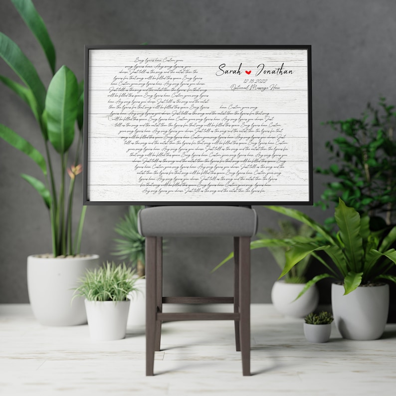 May include: A white wood sign with black calligraphy text that reads "Any song you hear,  I'll follow you,  Just like the song,  Wherever you go."  The sign also includes the names "Sarah & Jonathan" and the date "12.19.2022".