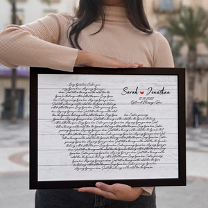 May include: A white wood-grain background with black cursive text that reads "Every love has a story..." and continues with a poem about love. The text is framed in a black frame. The names "Sarah" and "Jonathan" are written in black with a red heart between them. The date "12.10.2022" and the words "Our Wedding Date" are written below the names.