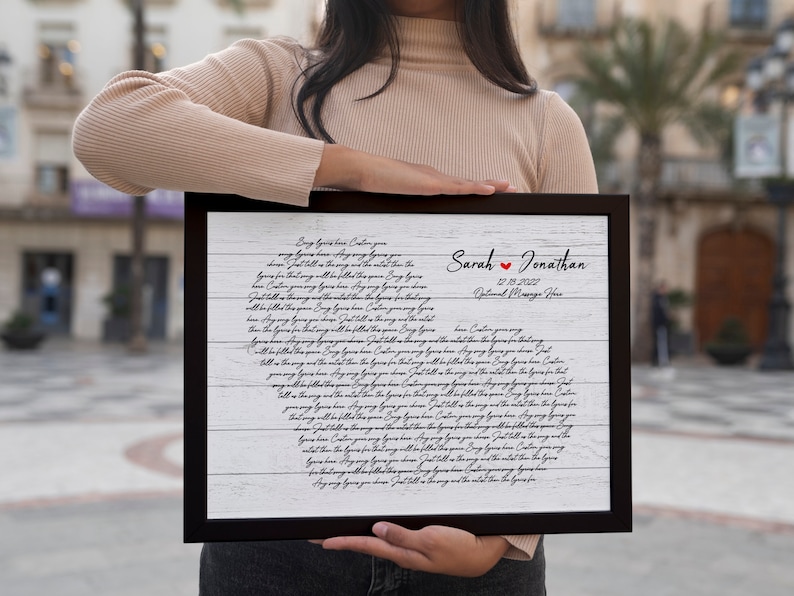 May include: A white wood-grain background with black cursive text that reads "Every love has a story..." and continues with a poem about love. The text is framed in a black frame. The names "Sarah" and "Jonathan" are written in black with a red heart between them. The date "12.10.2022" and the words "Our Wedding Date" are written below the names.