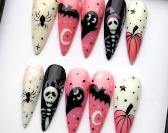 May include: Set of ten pink and white Halloween-themed press-on nails with various designs including a spider, a bat, a ghost, a skeleton, a pumpkin, and a crescent moon.