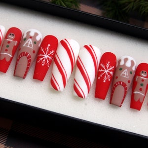Puede incluir: Conjunto de diez u&ntilde;as postizas con tem&aacute;tica de bast&oacute;n de caramelo rojo y blanco con dise&ntilde;os de casa de jengibre y hombre de jengibre.