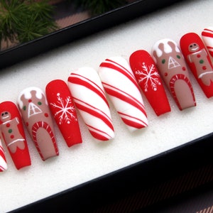 Puede incluir: Conjunto de diez u&ntilde;as postizas largas, rayadas de rojo y blanco como bastones de caramelo, con dise&ntilde;os de casa de jengibre y hombre de jengibre.