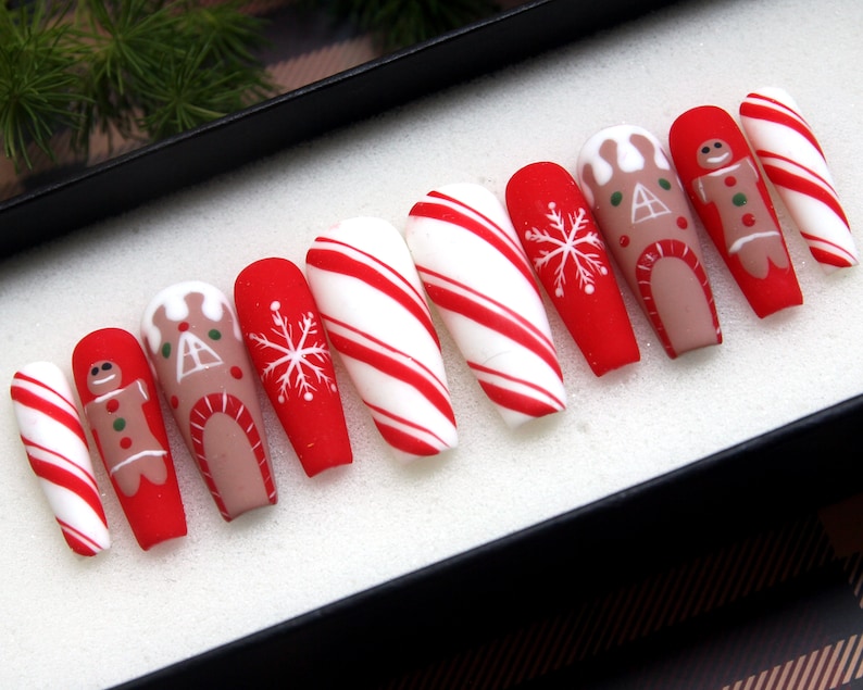 Puede incluir: Conjunto de diez u&ntilde;as postizas largas, rayadas de rojo y blanco como bastones de caramelo, con dise&ntilde;os de casa de jengibre y hombre de jengibre.