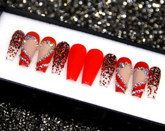 May include: Set of ten red coffin-shaped false nails with glitter and rhinestones. Some nails feature a heart design with rhinestones.