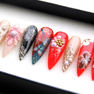 May include: A set of ten long, pointed, red, white, and black false nails with various designs, including butterflies, flowers, and glitter.