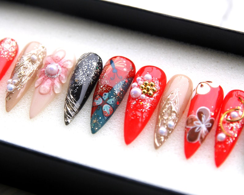 May include: A set of ten long, pointed, red, white, and black false nails with various designs, including butterflies, flowers, and glitter.