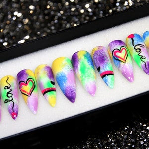 May include: Set of ten colorful, long, pointed false nails with a tie-dye design. Each nail has a different design, including hearts, swirls, and the word "love".