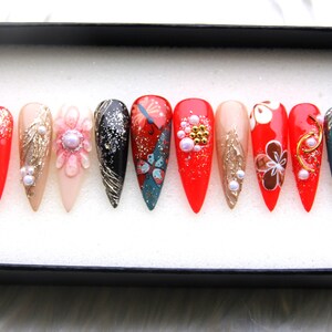May include: Set of ten false nails with various designs. The nails are red, black, gold, white, and blue with floral and butterfly patterns. Some nails have glitter and pearls.