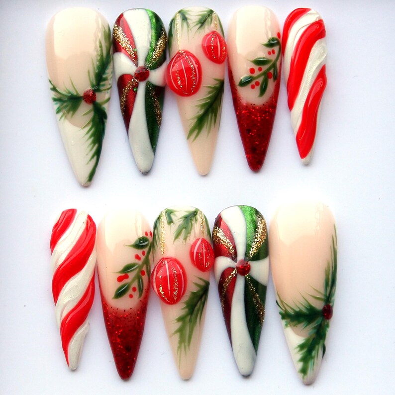 May include: A set of ten artificial nails with festive Christmas designs. The nails feature candy cane stripes, holly, red glitter, and ornaments. The color palette includes red, green, white, and gold, creating a holiday theme.