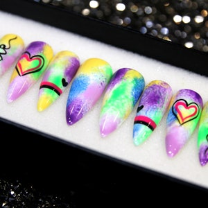 May include: Set of ten colorful, long, pointed false nails with a tie-dye design. Each nail has a different design, including hearts and the word "love".
