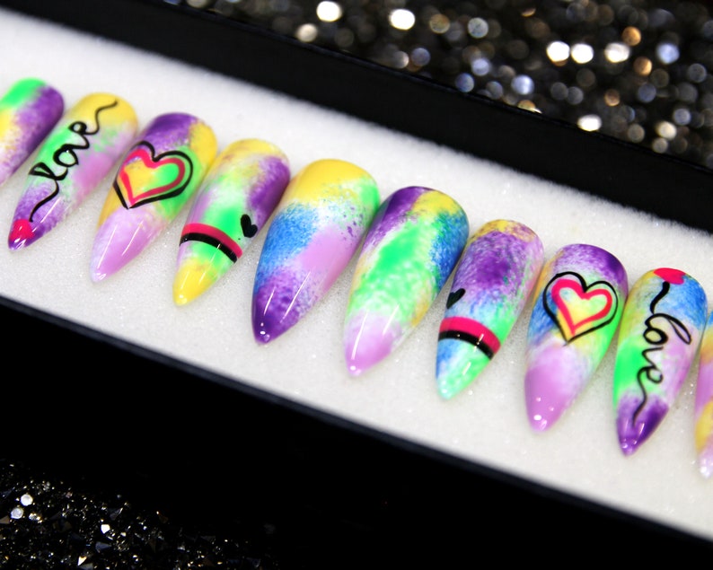 May include: Set of ten colorful, long, pointed false nails with a tie-dye design. Each nail has a different design, including hearts and the word "love".